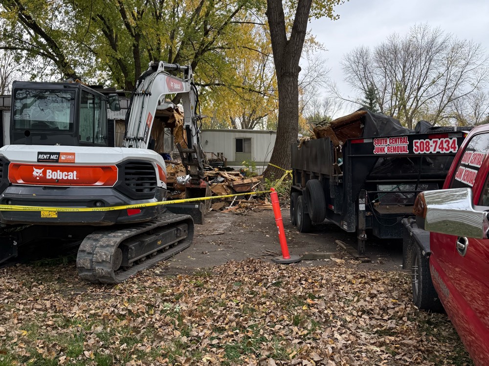 An excavator demolishing a home next to a South Central dump trailer loaded with debris