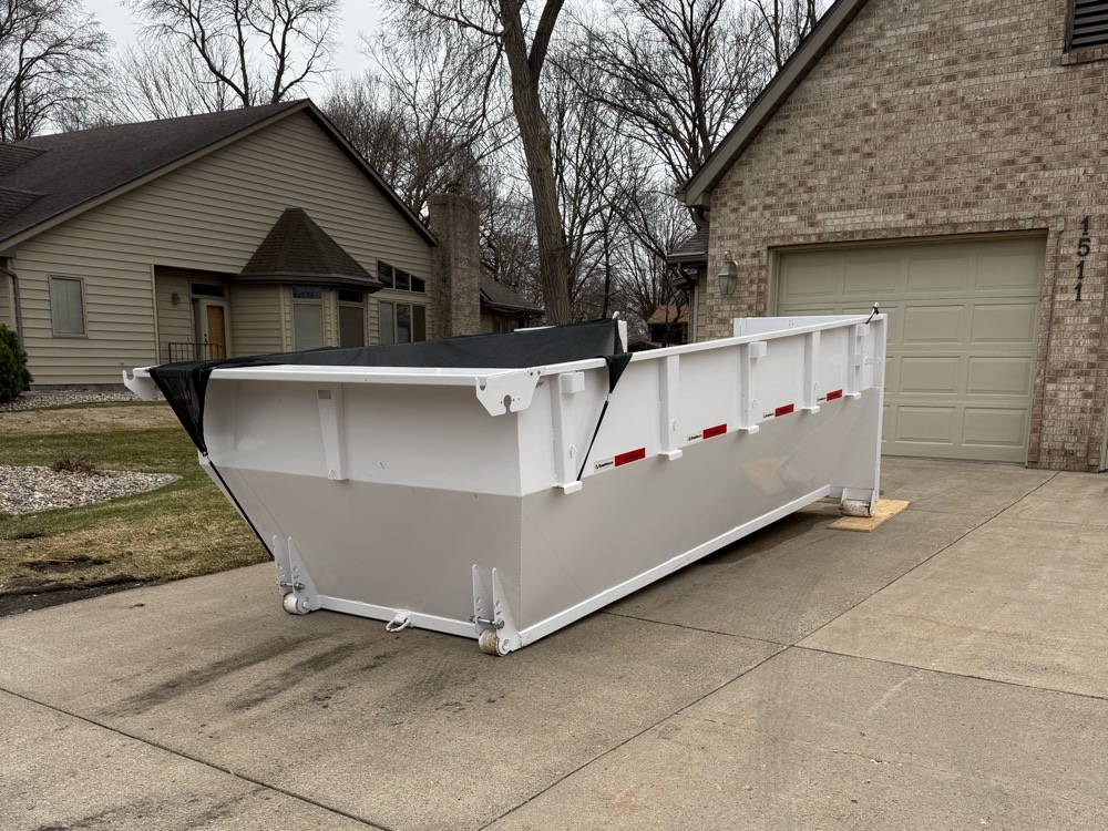 A white 15-yard dumpster dropped off in a residential driveway